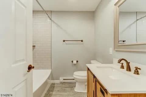 Bathroom with a white bathtub, toilet, and vanity with a light brown countertop. Light gray walls.