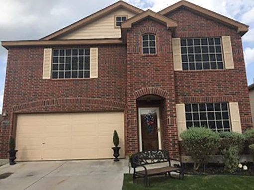 Two-story brick house with a beige garage door, arched entryway, and beige shutters, seen from a paved driveway.