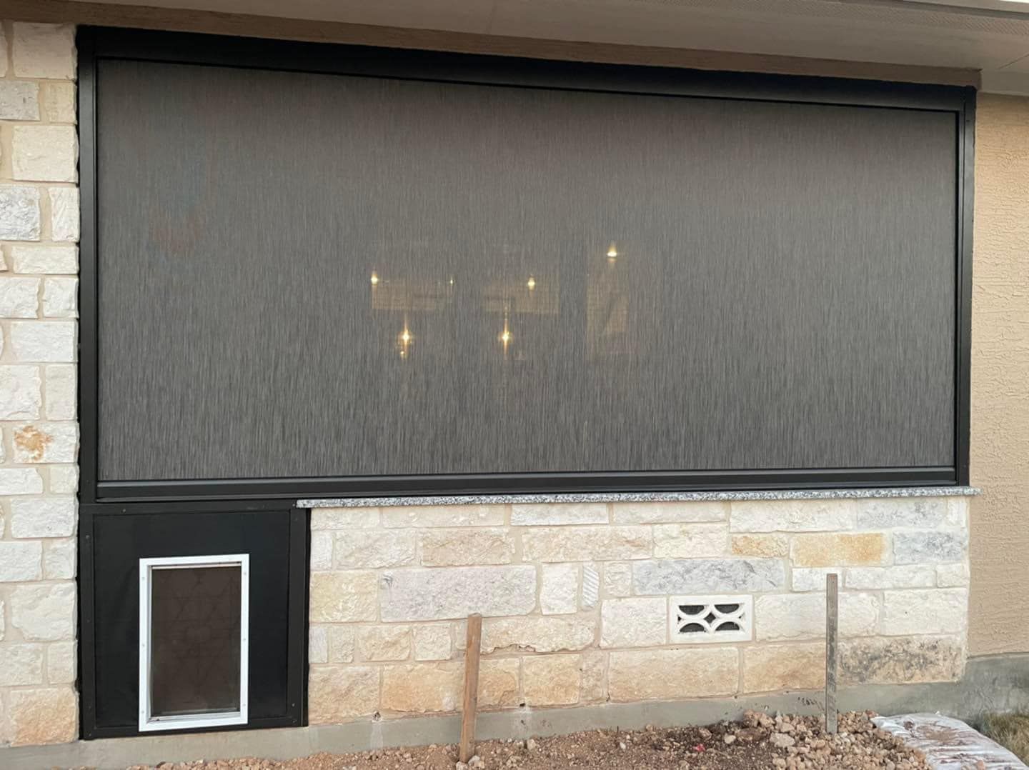 A large black outdoor solar screen installed on a stone wall next to a pet door.