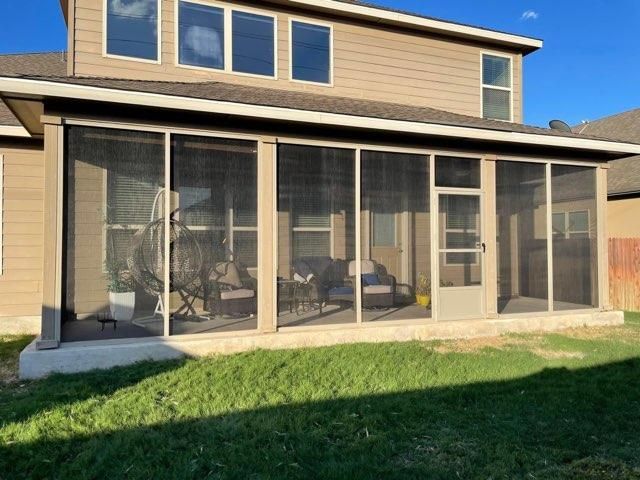 A tan screened-in porch with sliding doors, a red brick base, and patio furniture visible inside, set against a lawn.