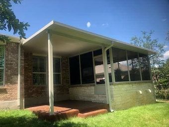 A brick house with a covered, screened-in patio area and a concrete floor on a sunny day with green grass in the foreground.
