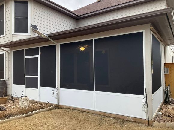 A house with a newly installed white-framed screened-in porch addition featuring dark mesh screens and a screen door.
