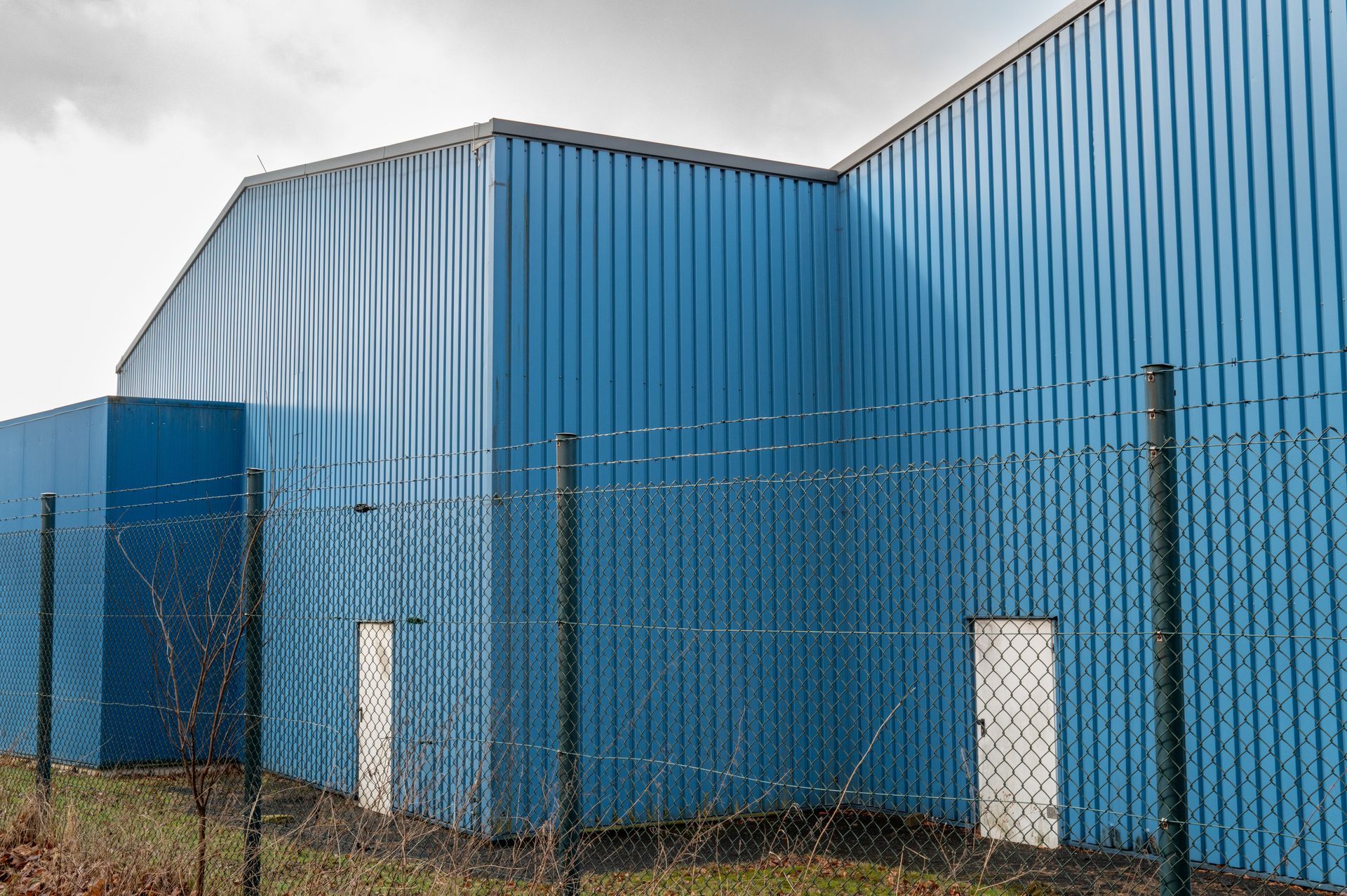Modern blue corrugated metal warehouse with security fence.