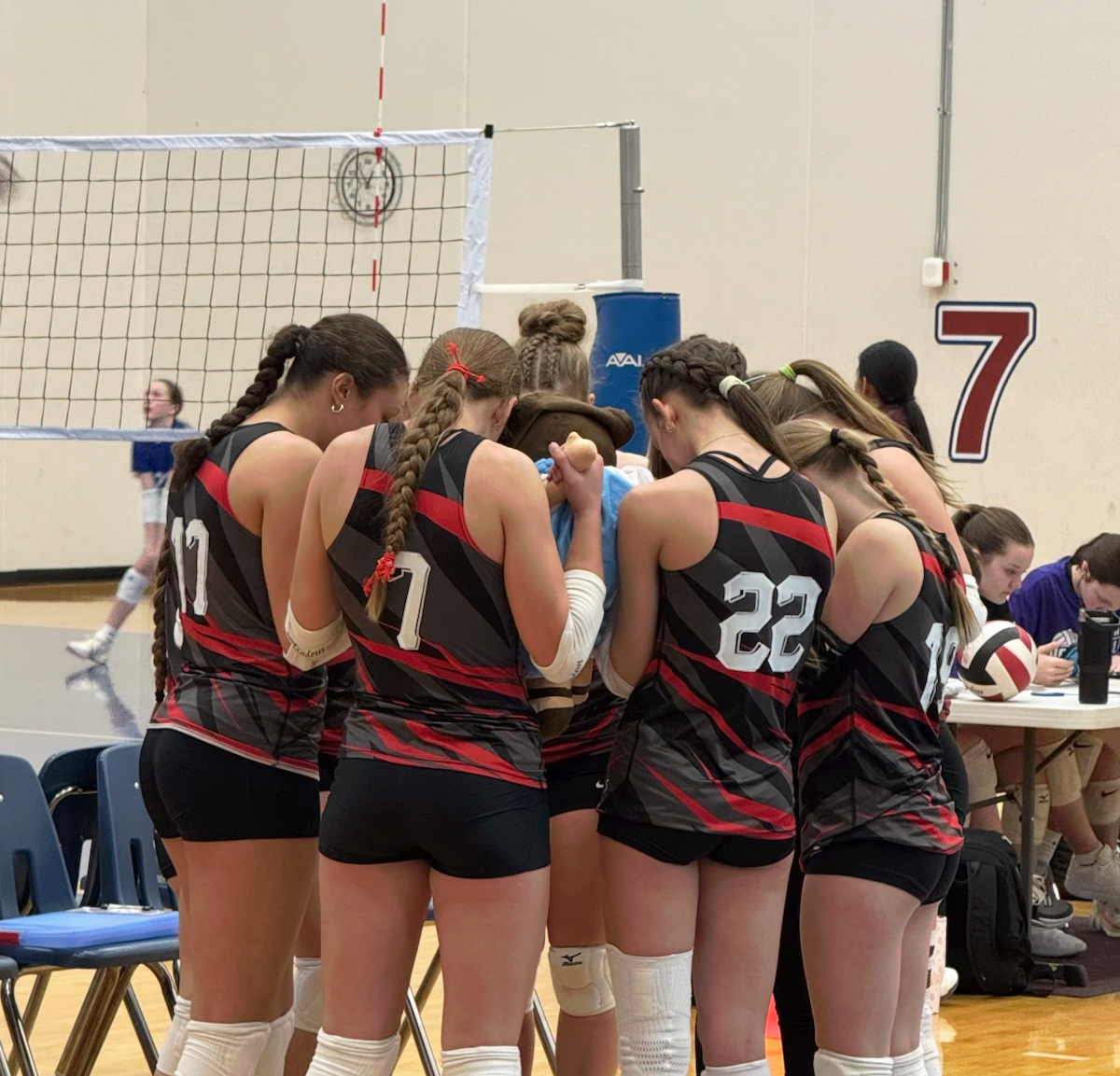 Volleyball player in teal jersey crouches ready on an indoor court during a match.
