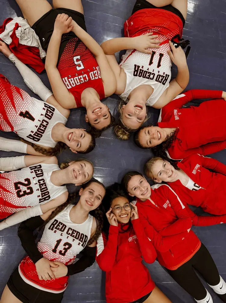Volleyball team in teal jerseys posing for a group photo against a white backdrop