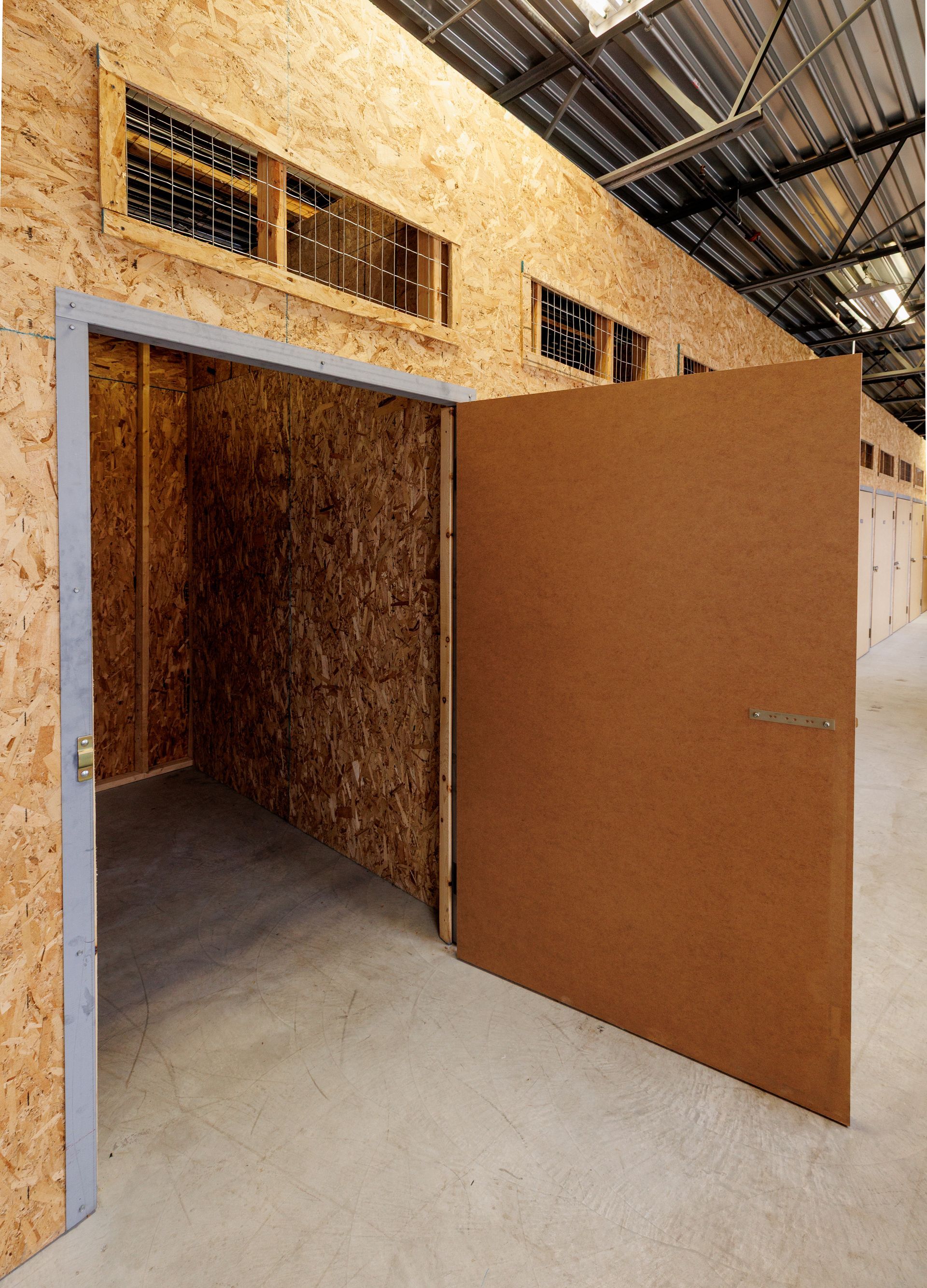Intérieur d'un box de stockage avec porte ouverte, réalisé en panneaux de bois, dans un entrepôt.