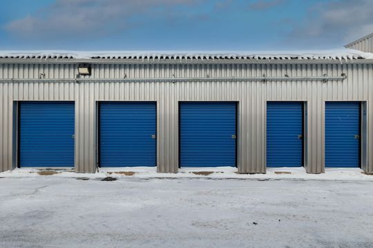 Portes bleues de box de stockage dans un parking enneigé sous un ciel nuageux.