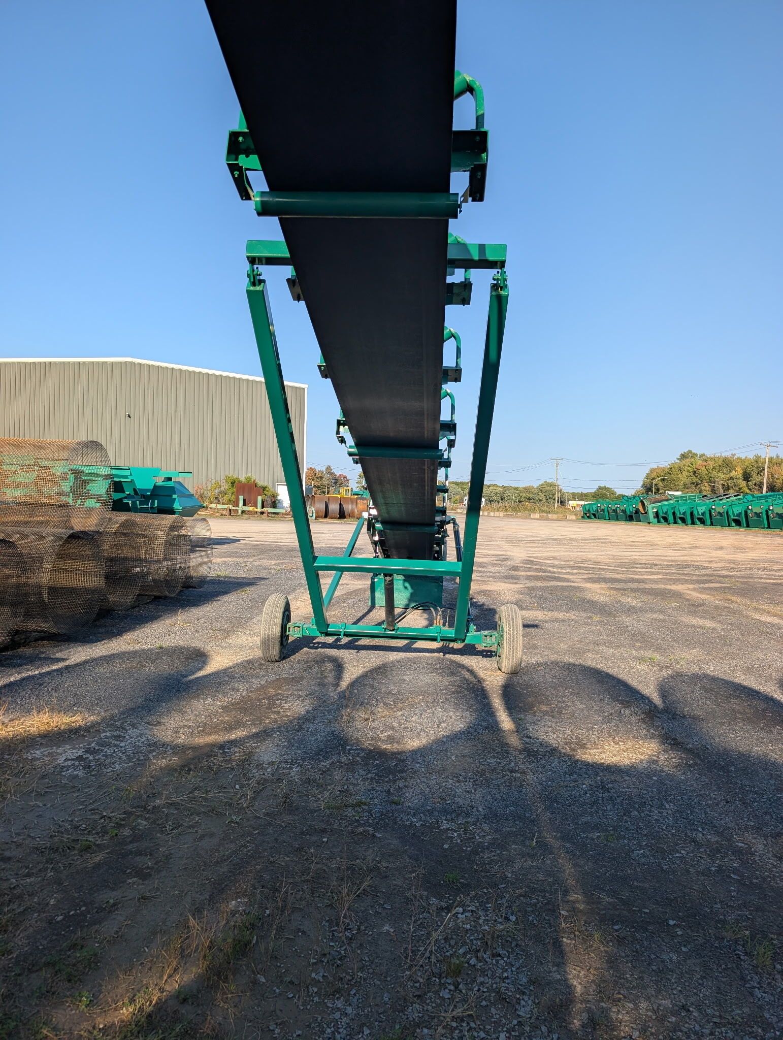 Green conveyor belt on a gravel surface under a blue sky, outside.