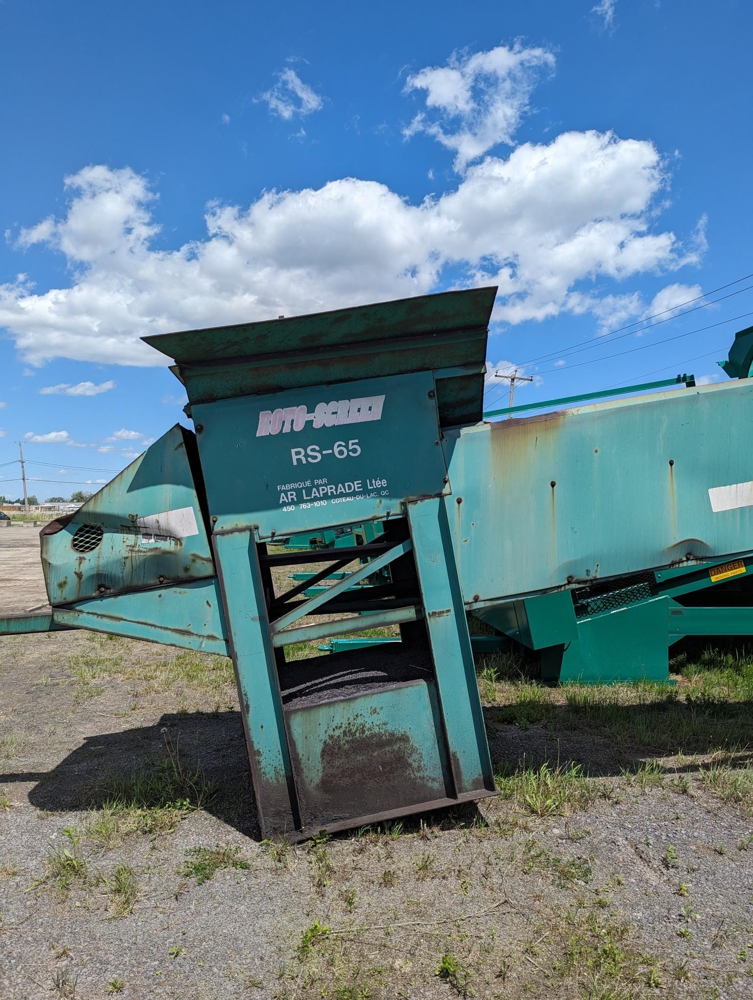 A green machine is sitting on top of a dirt field.