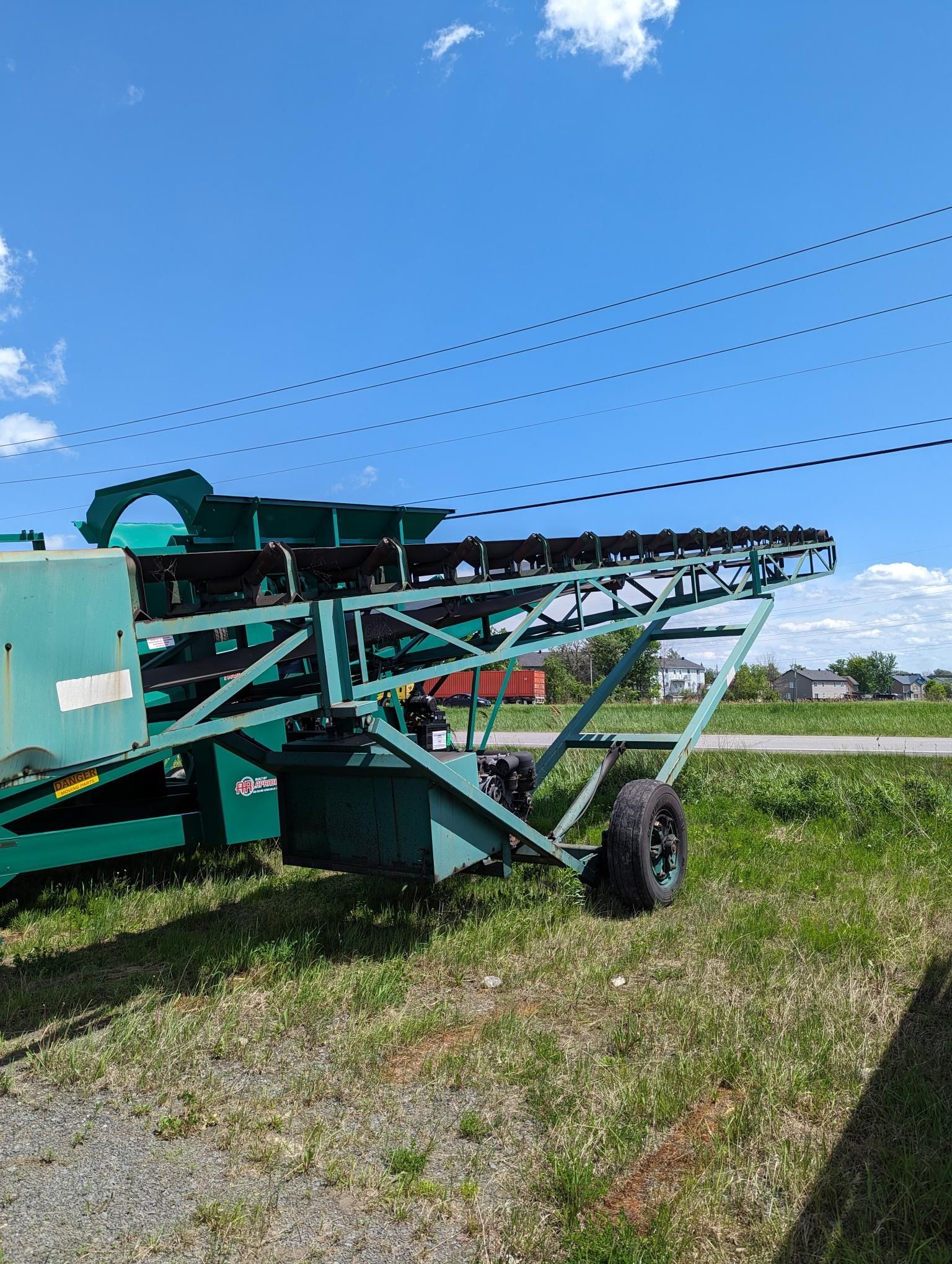 A green conveyor belt is parked in a grassy field.