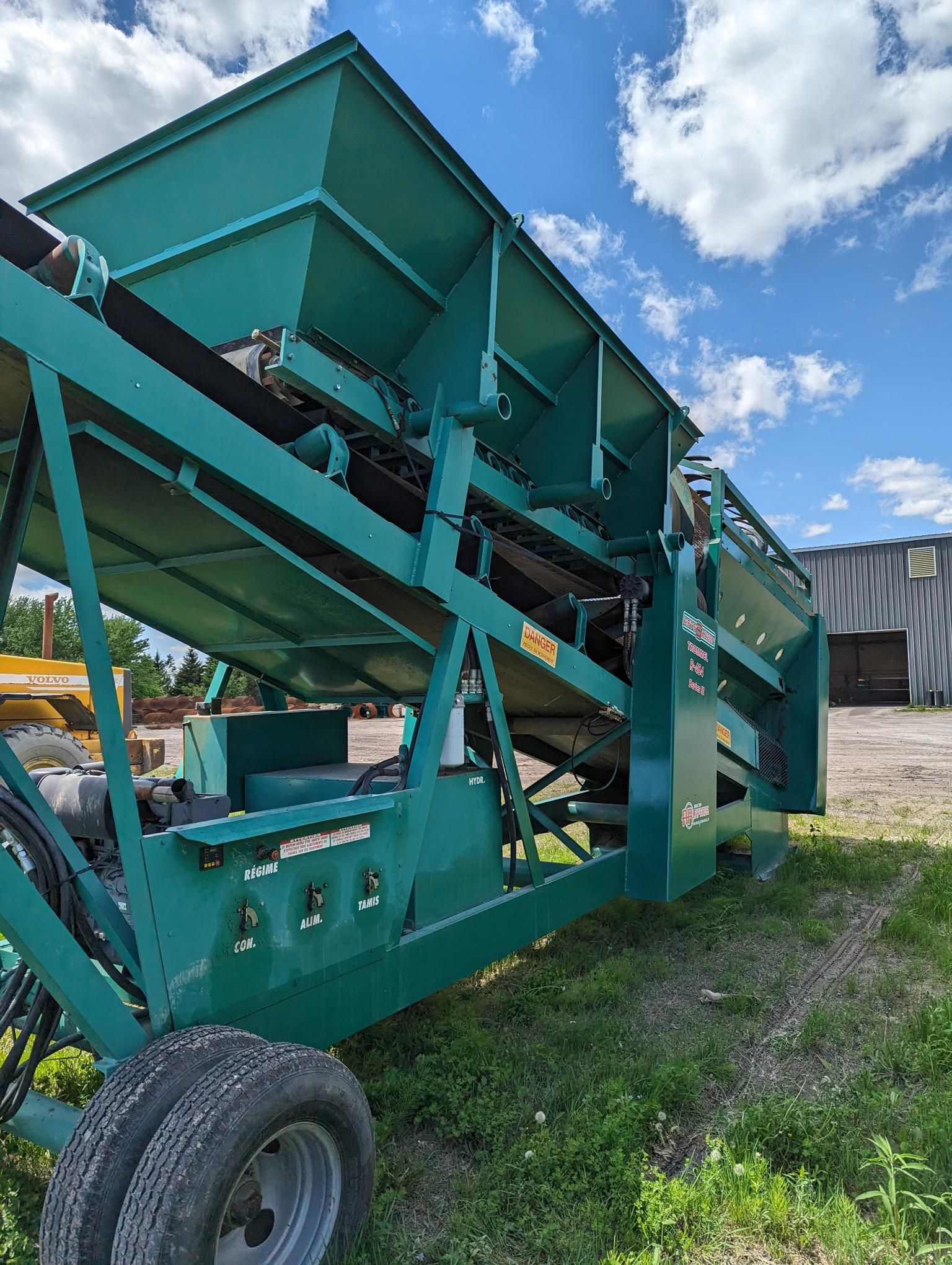 A green machine is parked in the grass in front of a building.