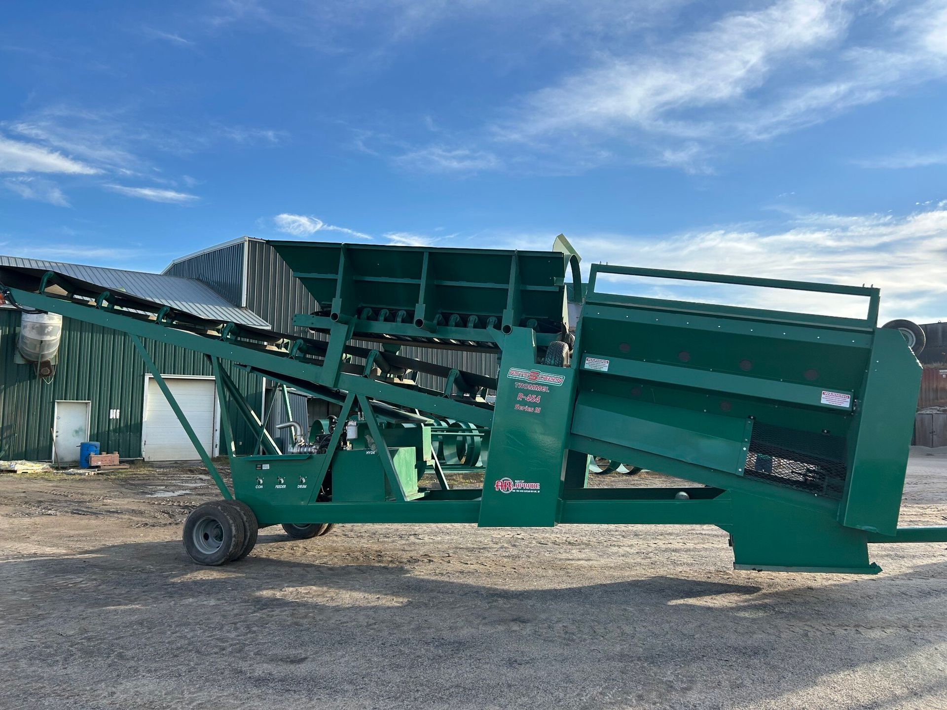 Green industrial sifter machine with conveyor belt, outdoors on a sunny day.