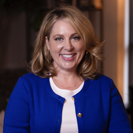 A woman in a blue jacket and white shirt is smiling for the camera.