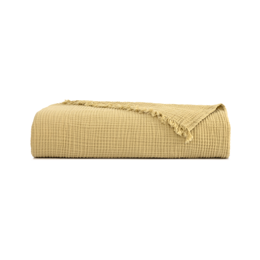 Un plaid jaune moutarde plié, à la texture rappelant la mousseline et aux bords effilochés, centré sur un fond blanc.
