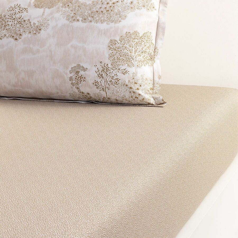 Linge de lit beige et doré à motifs, comprenant un oreiller à motif d'arbre.