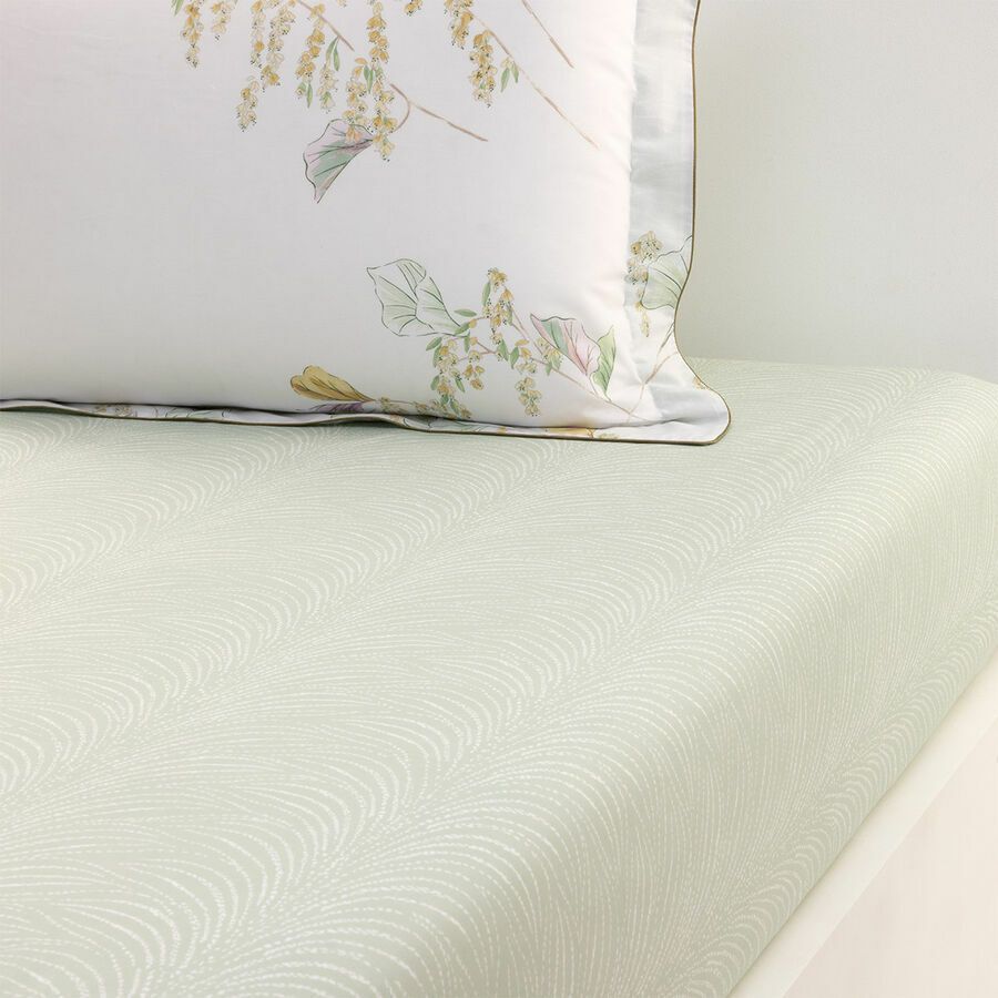 Oreiller blanc à motifs floraux sur un drap-housse vert clair à motifs.