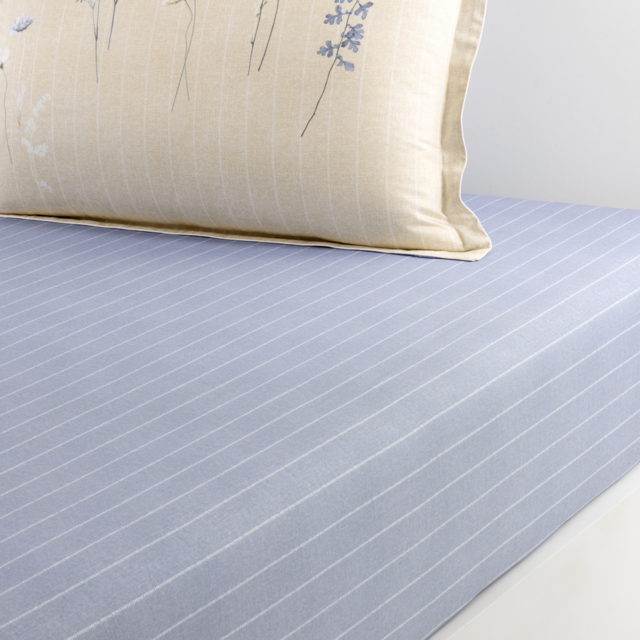 Un drap bleu clair à fines rayures blanches repose sous un oreiller couleur crème à motifs floraux bleus.