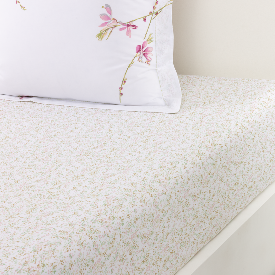 Un oreiller blanc brodé de fleurs roses repose sur un lit recouvert d'un drap à imprimé floral délicat et de couleur claire.