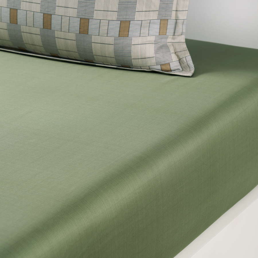 Un lit avec un drap vert et des oreillers dessus
