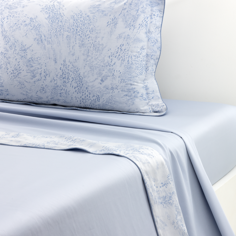 Gros plan sur un lit avec des draps bleu clair et un oreiller à motifs floraux blancs et bleus.