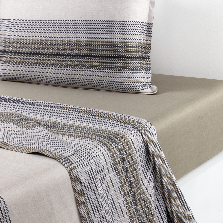 Un lit avec un drap-housse taupe, une couverture texturée à rayures grises et blanches et un oreiller à rayures assorti.