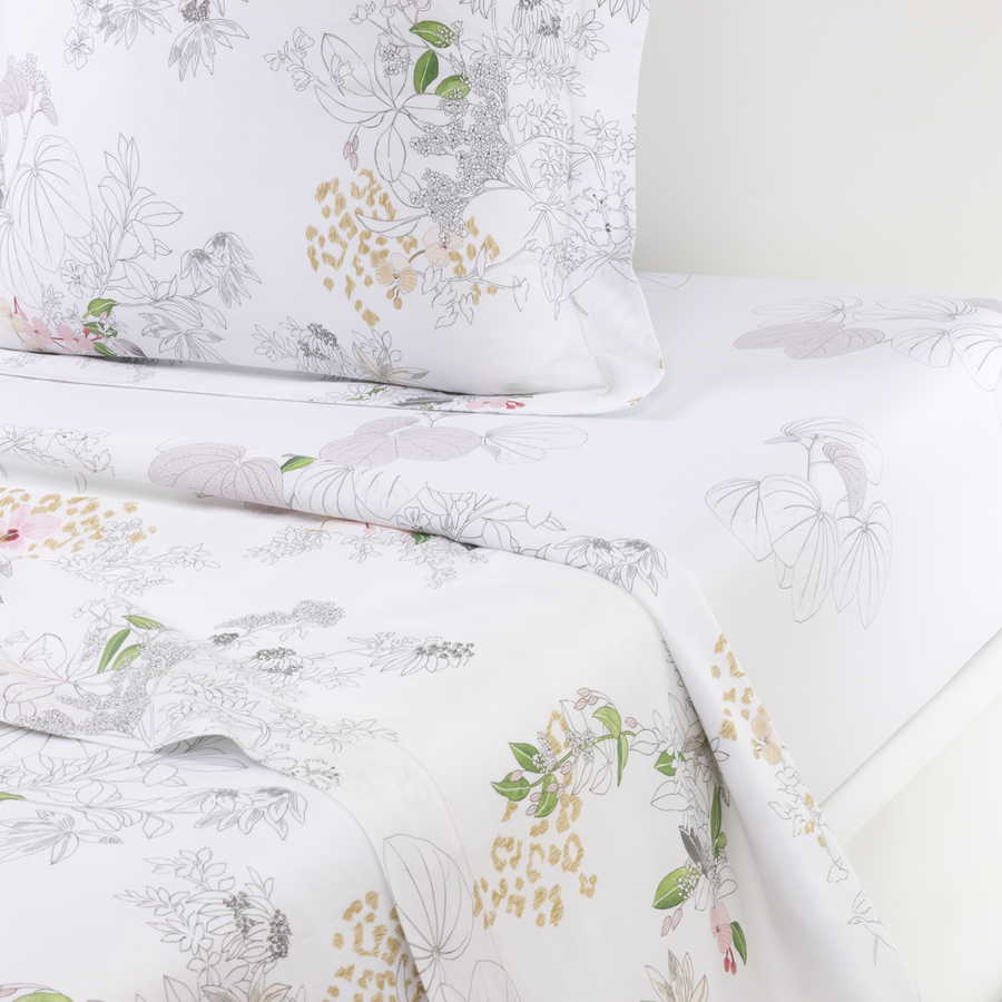 Une parure de lit blanche pliée, ornée d'un imprimé botanique doux avec des fleurs grises esquissées, des feuilles vertes et des touches dorées.