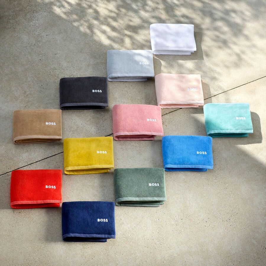 Une collection de serviettes rectangulaires pliées, de couleurs unies variées, chacune portant la marque « BOSS » imprimée sur le bord.