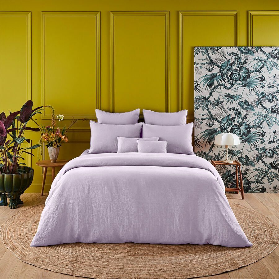 Un lit avec une couette et des oreillers violets dans une pièce aux murs jaunes.