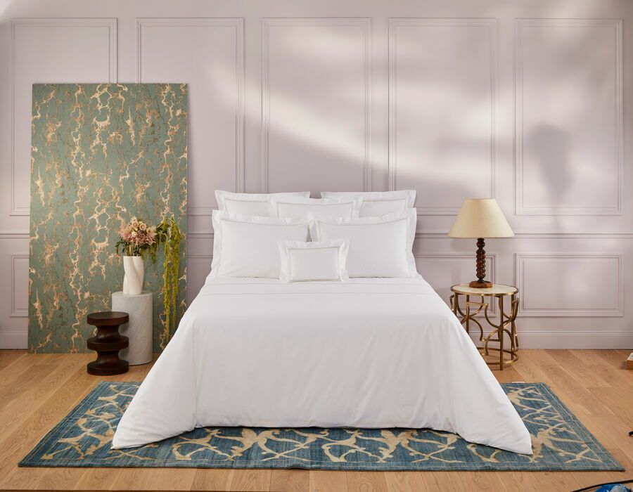 Un lit avec des draps blancs et des oreillers est posé sur un tapis dans une chambre.