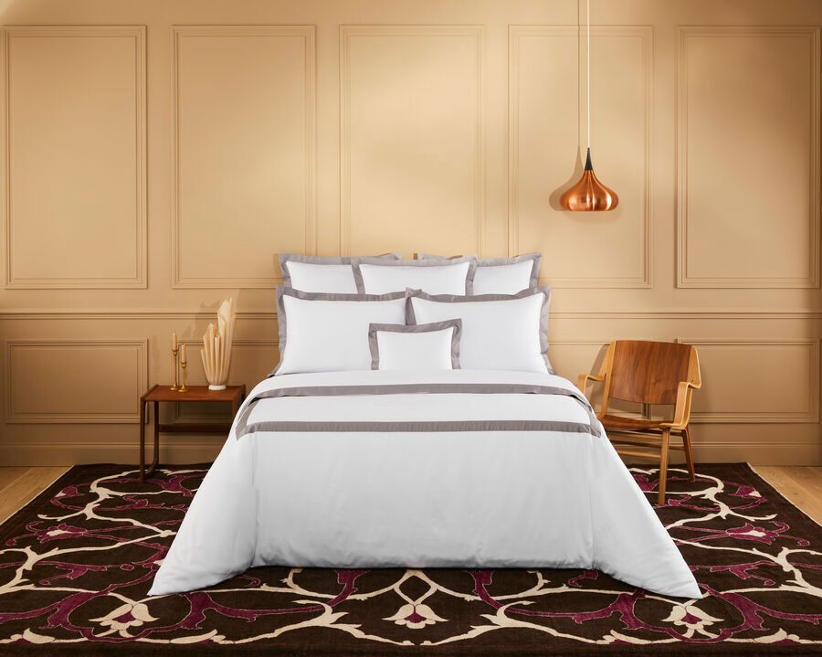 Chambre avec literie blanche, moulures marron, éléments en bois et tapis à motifs.