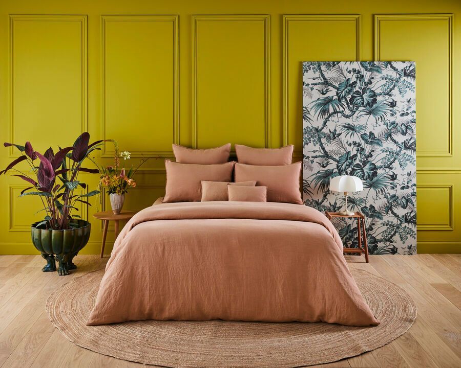 Un lit avec une couette et des oreillers roses dans une chambre aux murs jaunes.