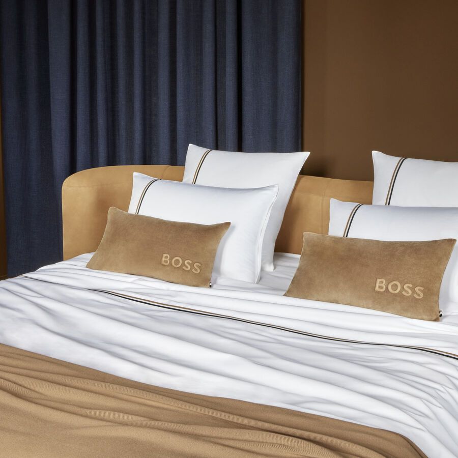Un lit avec des draps blancs et des oreillers marron sur lesquels est écrit