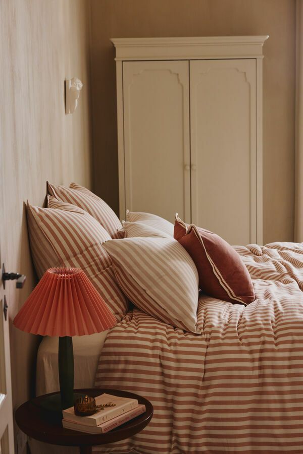 Chambre confortable avec linge de lit à rayures, armoire crème et lampe rouge sur la table de chevet