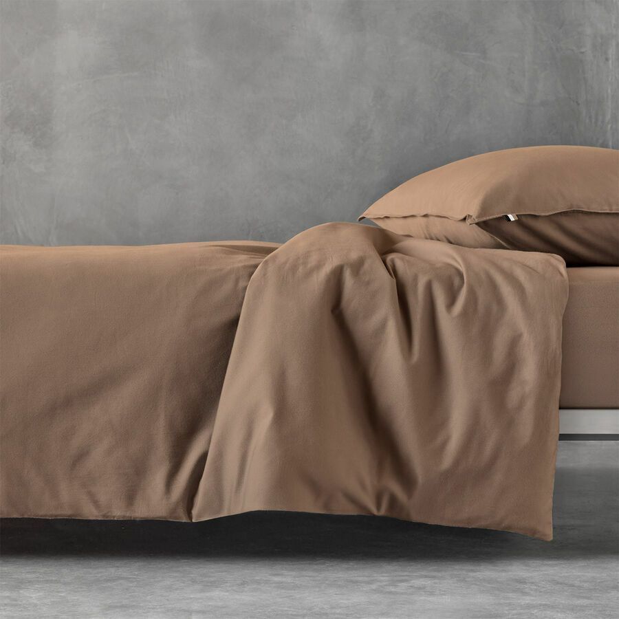Gros plan sur un lit avec une housse de couette aux tons chauds bruns et un oreiller assorti, devant un mur gris texturé.