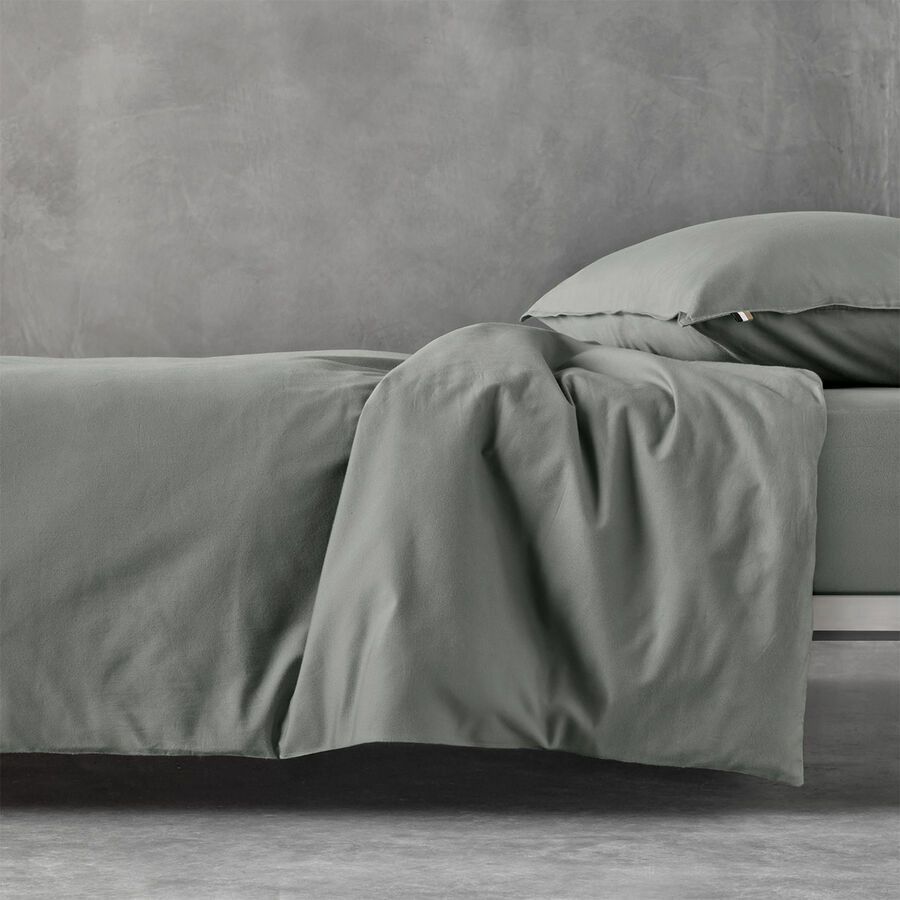 Un lit gris avec une housse de couette et une taie d'oreiller, adossé à un mur texturé gris assorti.