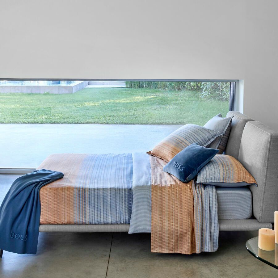 Un lit avec une couette rayée et des oreillers devant une fenêtre