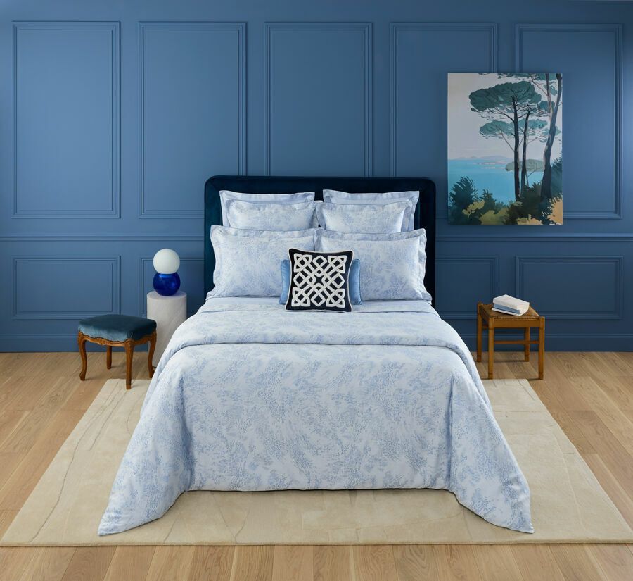 Un lit avec des draps à motifs bleu clair, une tête de lit bleu foncé et un coussin décoratif bleu, le tout devant un mur lambrissé bleu.