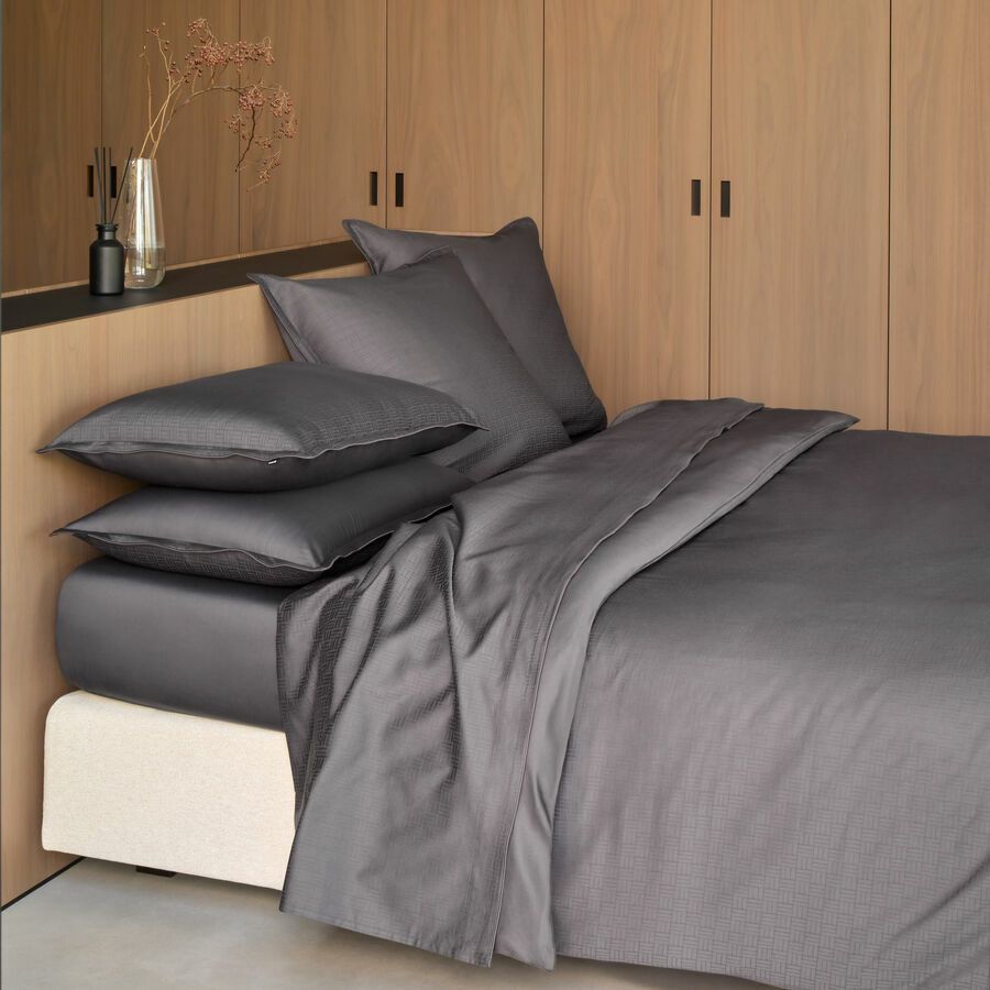 Un lit avec des draps et des oreillers gris foncé, adossé à un mur lambrissé de bois clair avec des placards intégrés.