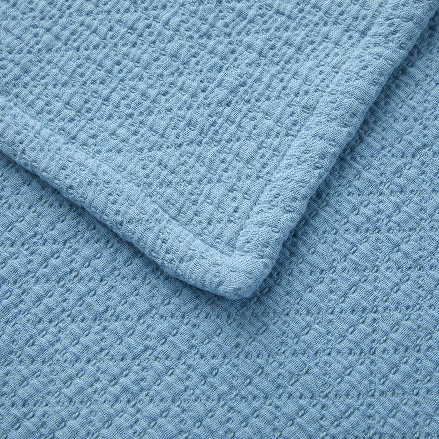Gros plan sur une couverture bleu clair en tissu gaufré texturé à petits points et bordée de surpiqûres.