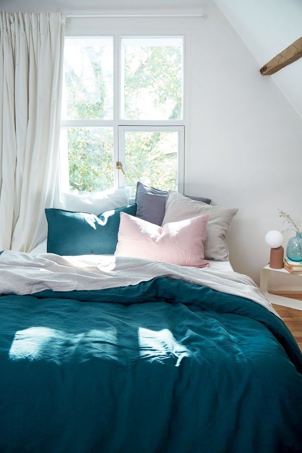 Un lit avec une couette et des oreillers bleus dans une chambre à côté d'une fenêtre.