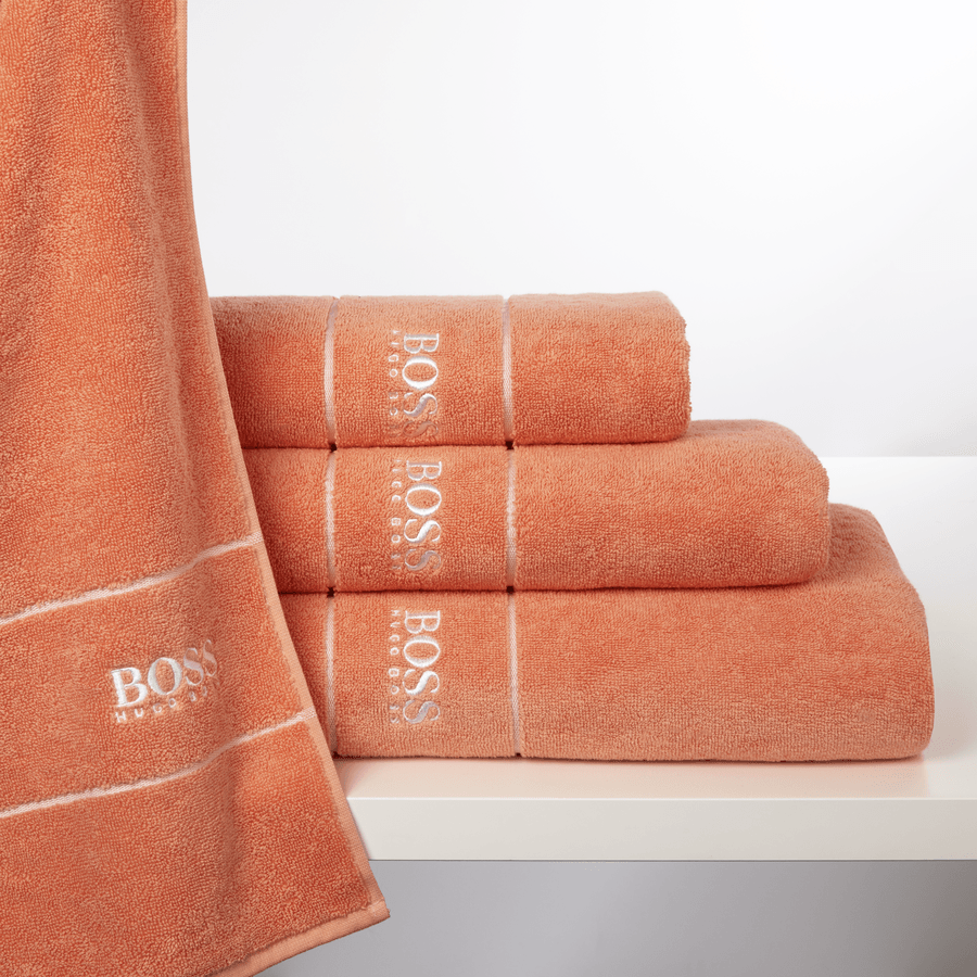 Trois serviettes orange sont empilées les unes sur les autres sur une étagère blanche.