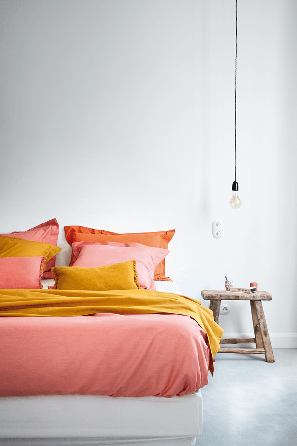Un lit avec une couette rose et des oreillers jaunes dans une chambre.