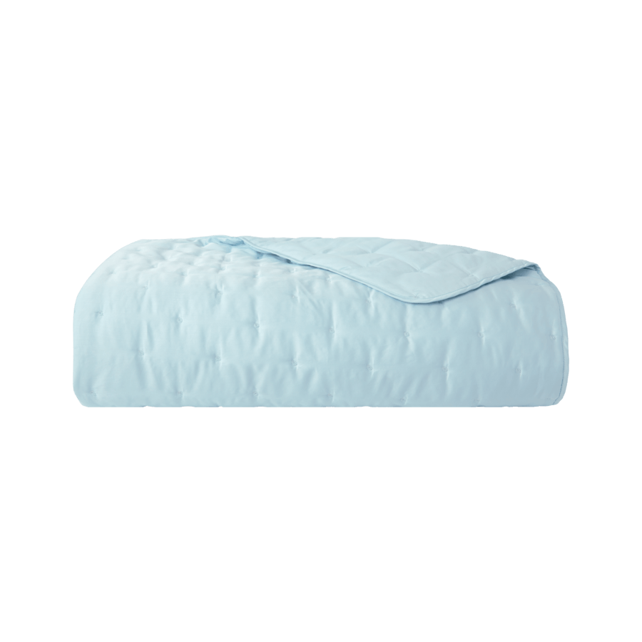 Une courtepointe bleu clair est posée sur un lit sur un fond blanc.