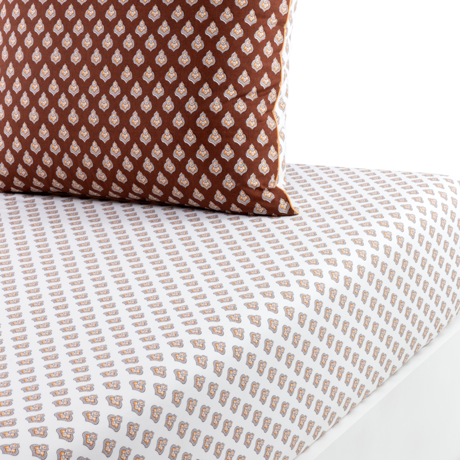 Un coussin décoratif marron à motifs floraux blancs posé sur un drap-housse orné du même motif, mais en plus petit.