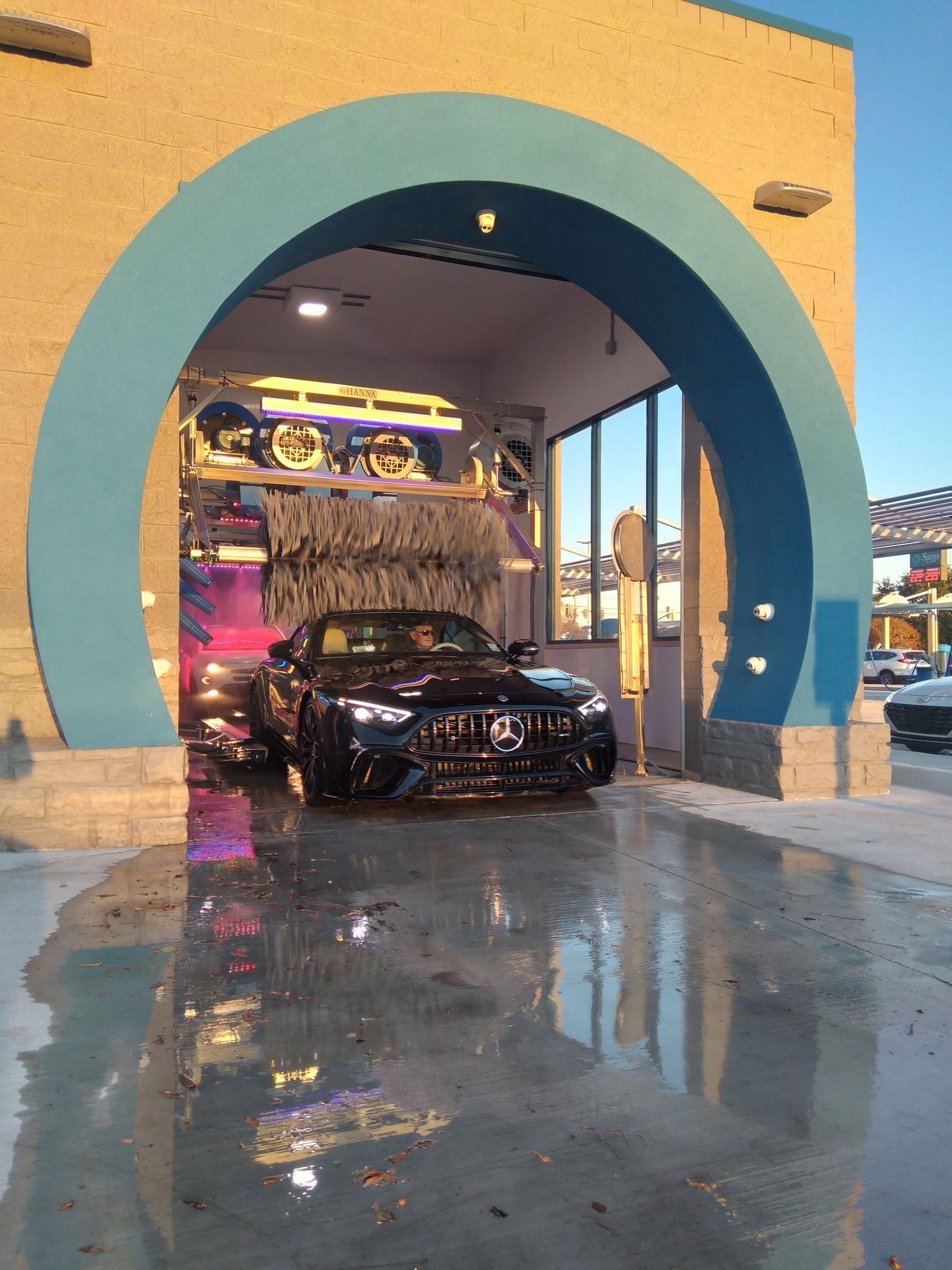 Black sports car parked under a blue archway outside a building at sunset