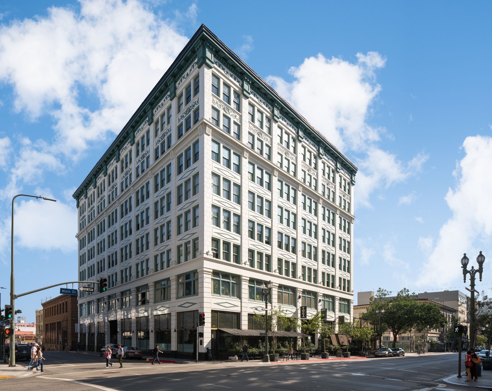 Tall white office building with many windows on a city street under a blue sky with clouds
