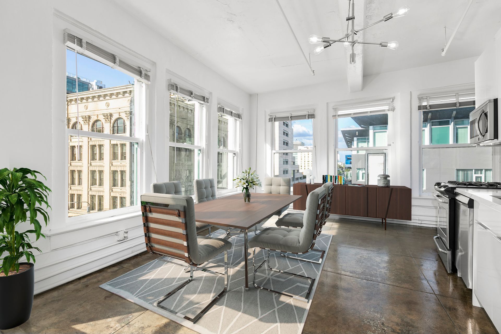 Bright modern dining area with large windows, wooden table, chairs, rug, and kitchen view