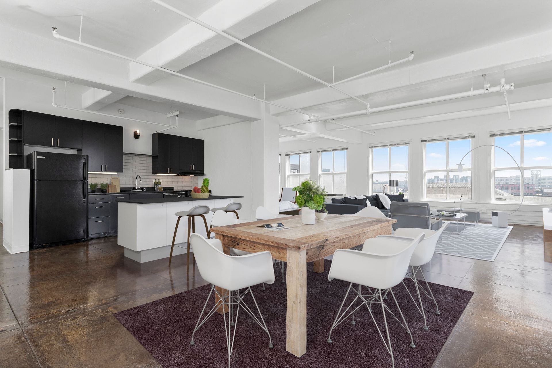 Bright open-plan kitchen and dining area with white furniture, dark floor, and large windows.