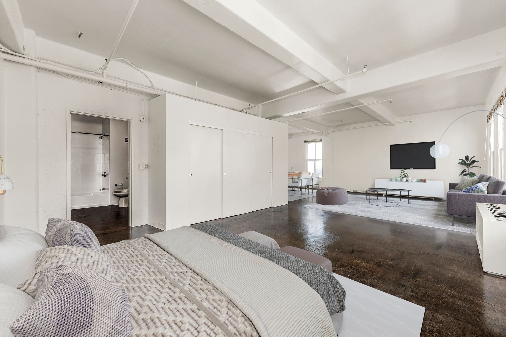 Bright modern loft living room with white walls, dark wood floors, gray sofa, and wall-mounted TV