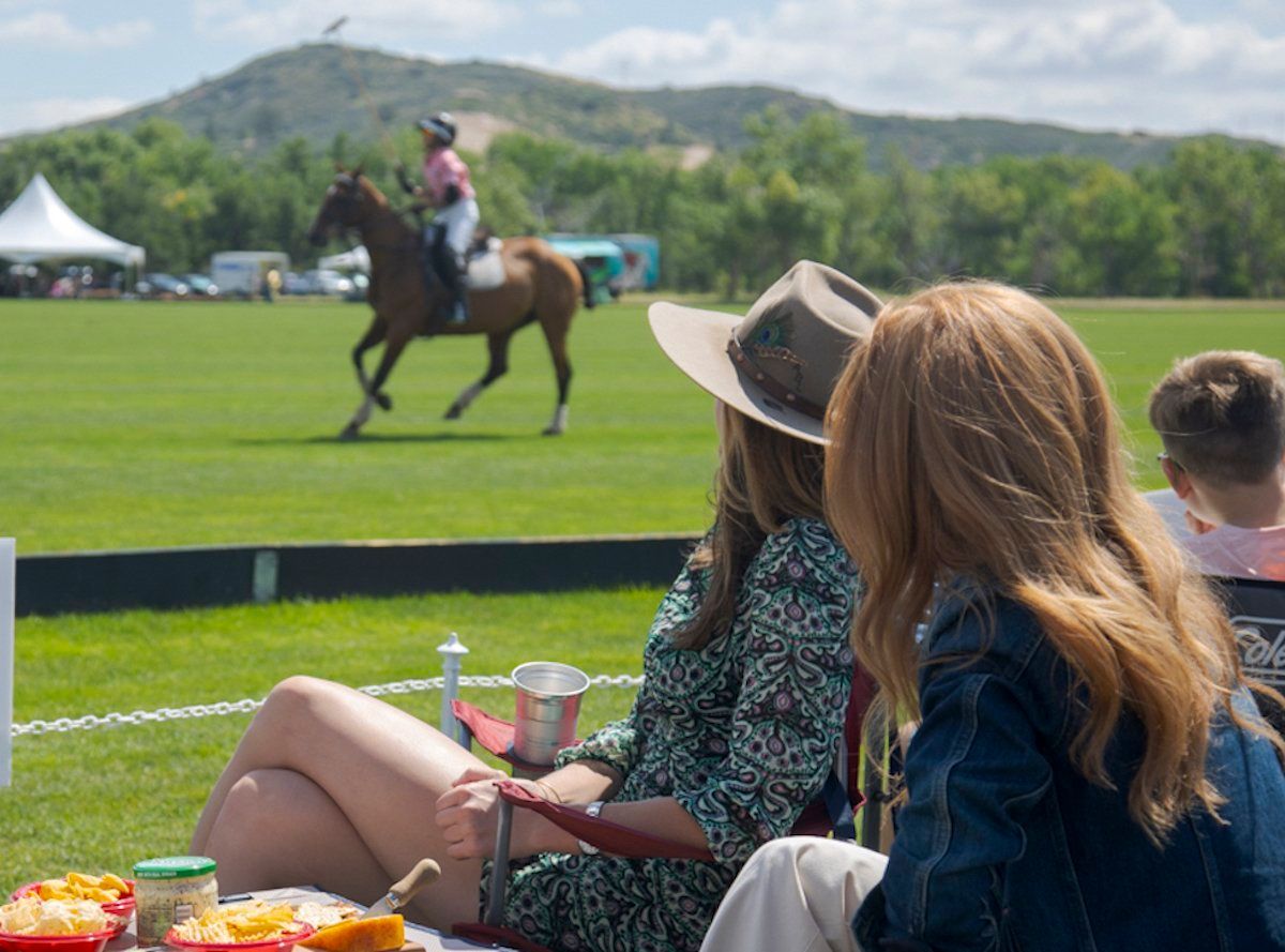 Two women are sitting on the grass watching a horse race
